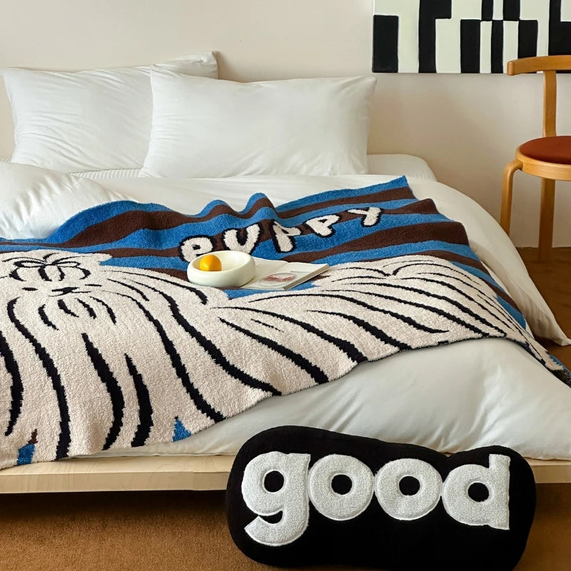 Une couverture de lit douillette dans des tons bleu et marron avec un motif rayé et un coussin décoratif avec l'inscription "good".