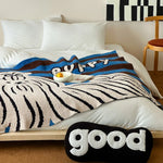 Une couverture de lit douillette dans des tons bleu et marron avec un motif rayé et un coussin décoratif avec l'inscription "good".