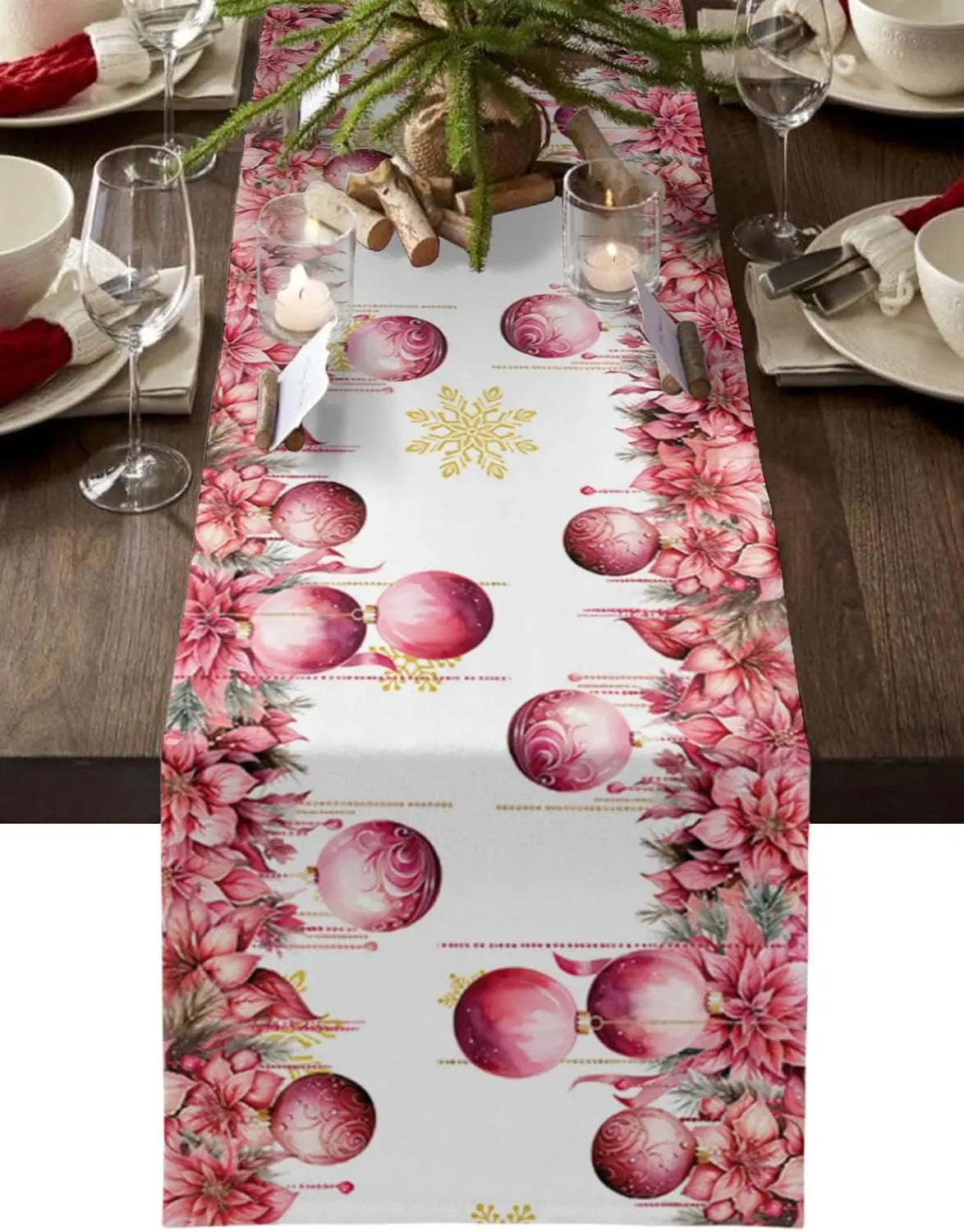 Table de fête décorée de décorations de Noël en rose et de bougies, sur un chemin de table à motifs de boules de Noël rose et de fleurs roses.