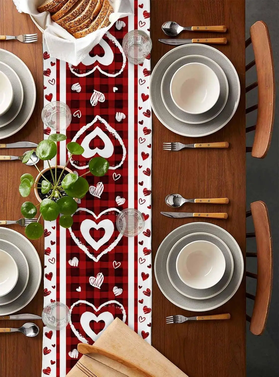La table est élégamment dressée avec des assiettes blanches, des couverts en bois et des décorations rouges à motifs de cœurs, créant une ambiance conviviale et romantique.