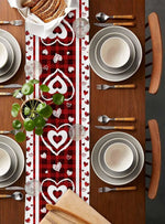 La table est élégamment dressée avec des assiettes blanches, des couverts en bois et des décorations rouges à motifs de cœurs, créant une ambiance conviviale et romantique.