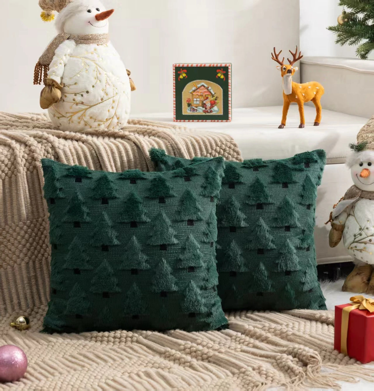 Coussin décoratif vert à motifs d'arbres de Noël, entouré de jouets et de décorations saisonnières sur un canapé douillet.