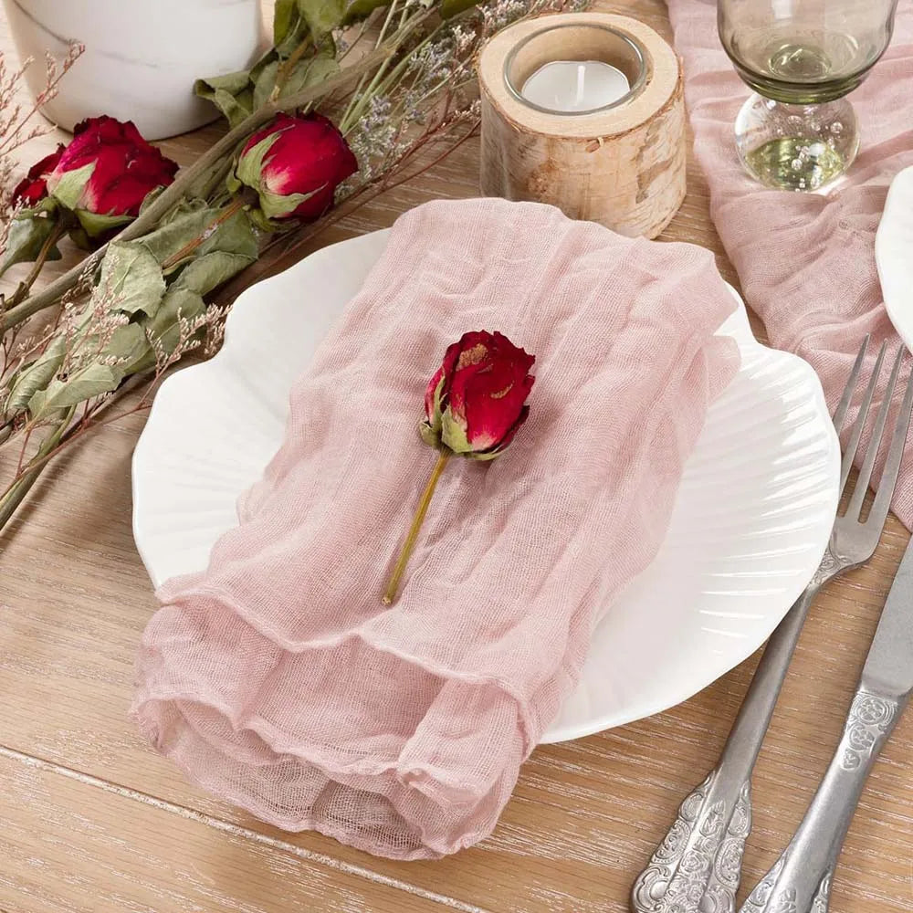 Une décoration de table romantique avec de belles roses rouges sur une serviette rose pâle, entourée de bougies dans un décor naturel.