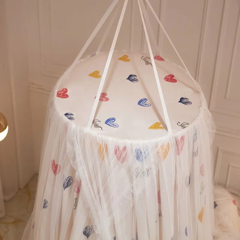Lit à baldaquin blanc avec motifs de coeurs colorés, créant un environnement douillet et décoratif pour une chambre d'enfant.