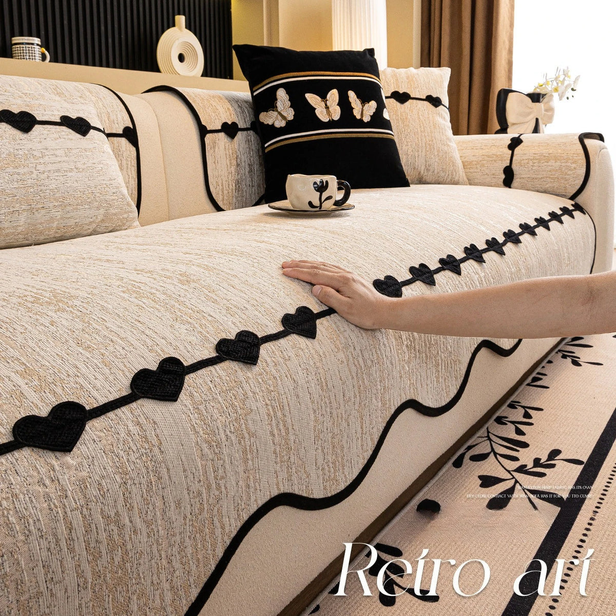 Une belle chambre élégante ornée de motifs de papillons et de cœurs noirs sur une couverture beige, avec des coussins assortis et une tasse décorative, créant une atmosphère chaleureuse et sophistiquée.