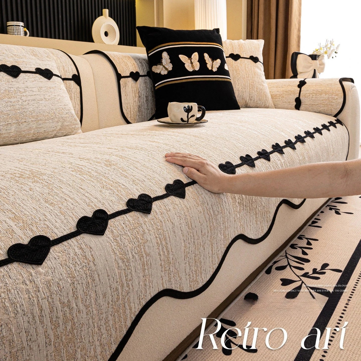 Une belle chambre élégante ornée de motifs de papillons et de cœurs noirs sur une couverture beige, avec des coussins assortis et une tasse décorative, créant une atmosphère chaleureuse et sophistiquée.