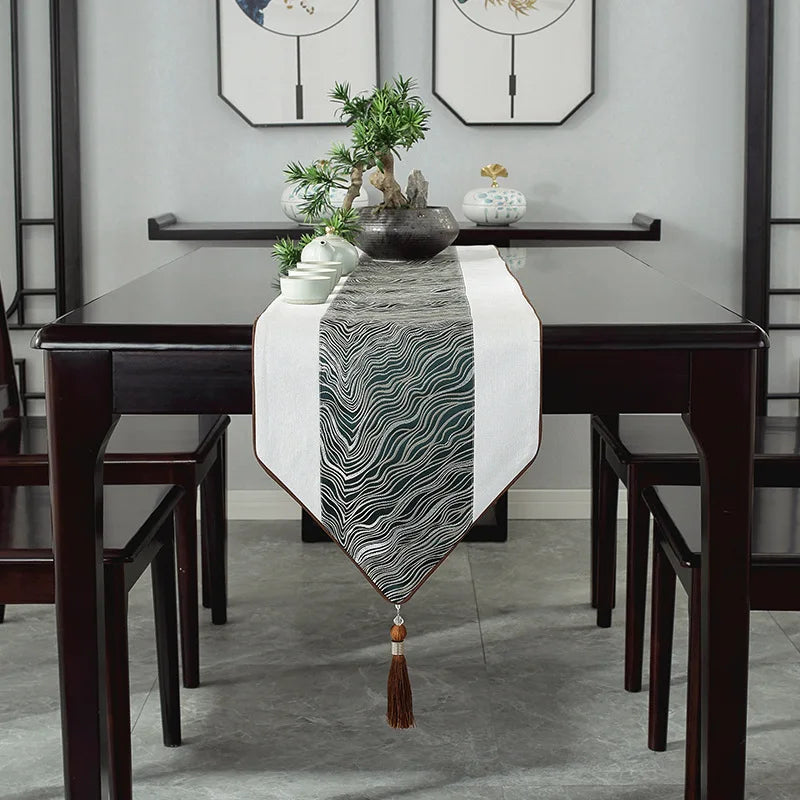 L'image montre une élégante table à manger en bois foncé avec un chemin de table décoratif orné de motifs graphiques, accompagnée de plantes vertes et d'accessoires dans un style épuré et moderne.