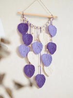 Un joli mobile fait de feuilles macramé violettes et blanches, suspendu à un cadre en bois, crée une décoration murale apaisante et élégante.