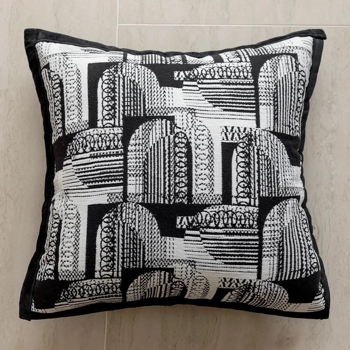 Cette image présente un coussin décoratif avec un motif géométrique en noir et blanc, composé de lignes, de formes et de textures abstraites.