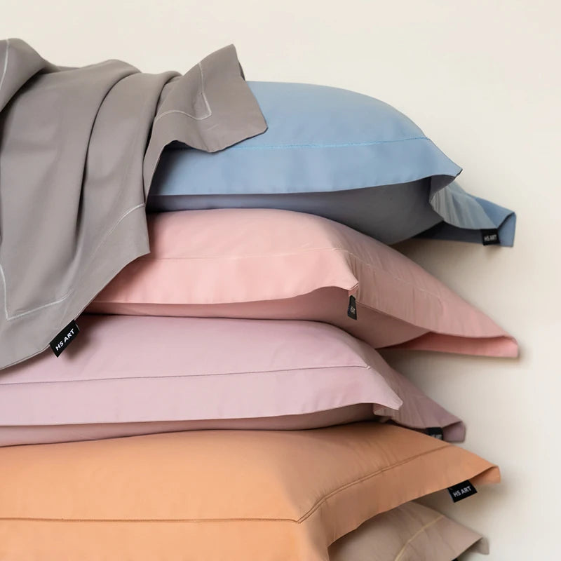 L'image montre un tas de coussins de différentes couleurs pastel, notamment des teintes grise, rose et orange, formant un motif intéressant et texturé.