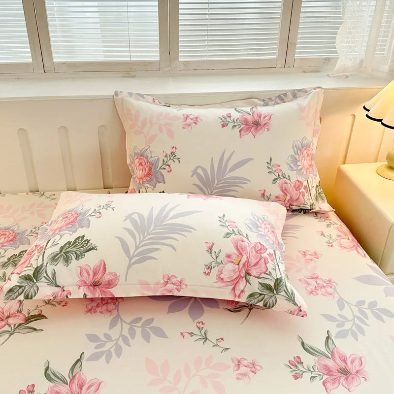 Parure de lit à motifs floraux roses et gris, avec des coussins assortis et un grand décor vintage floral sur un fond clair dans une pièce lumineuse.