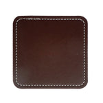 Image d'un carré en cuir marron foncé avec coutures blanches apparentes sur les bords, utilisé comme accessoire de bureau ou de décoration.