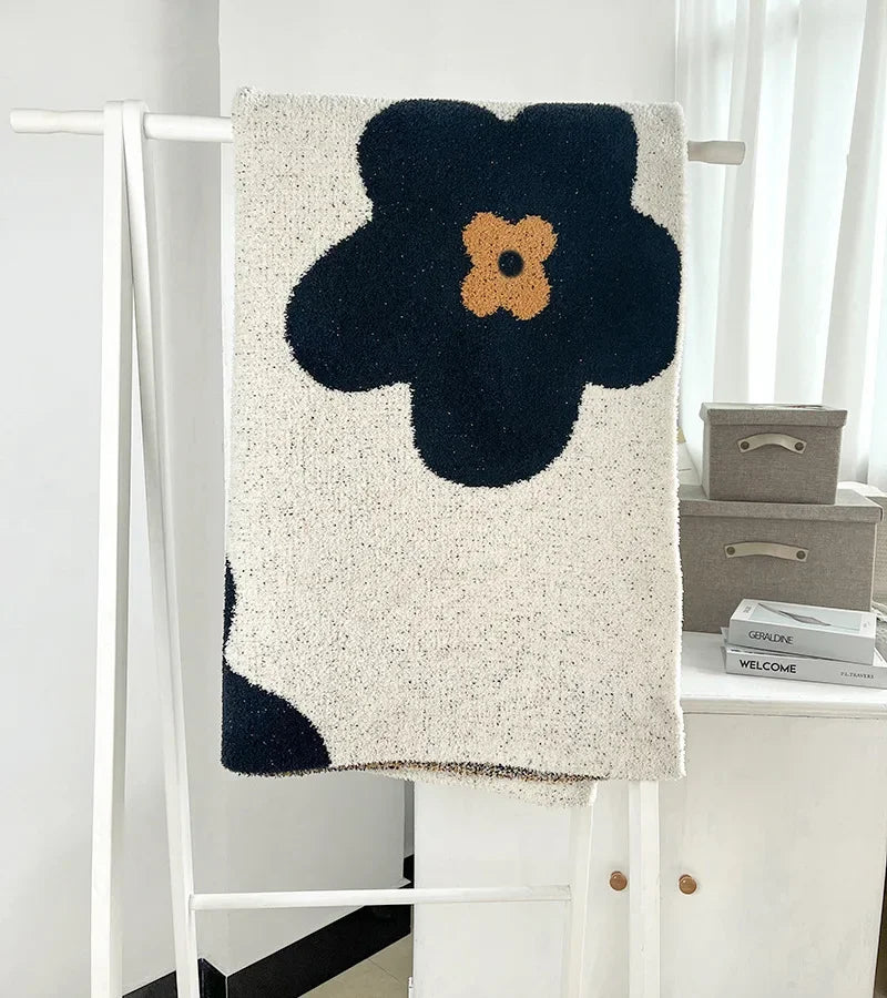 Tapis blanc et noir avec une fleur jaune, suspendu sur un portant en métal blanc dans une pièce lumineuse.
