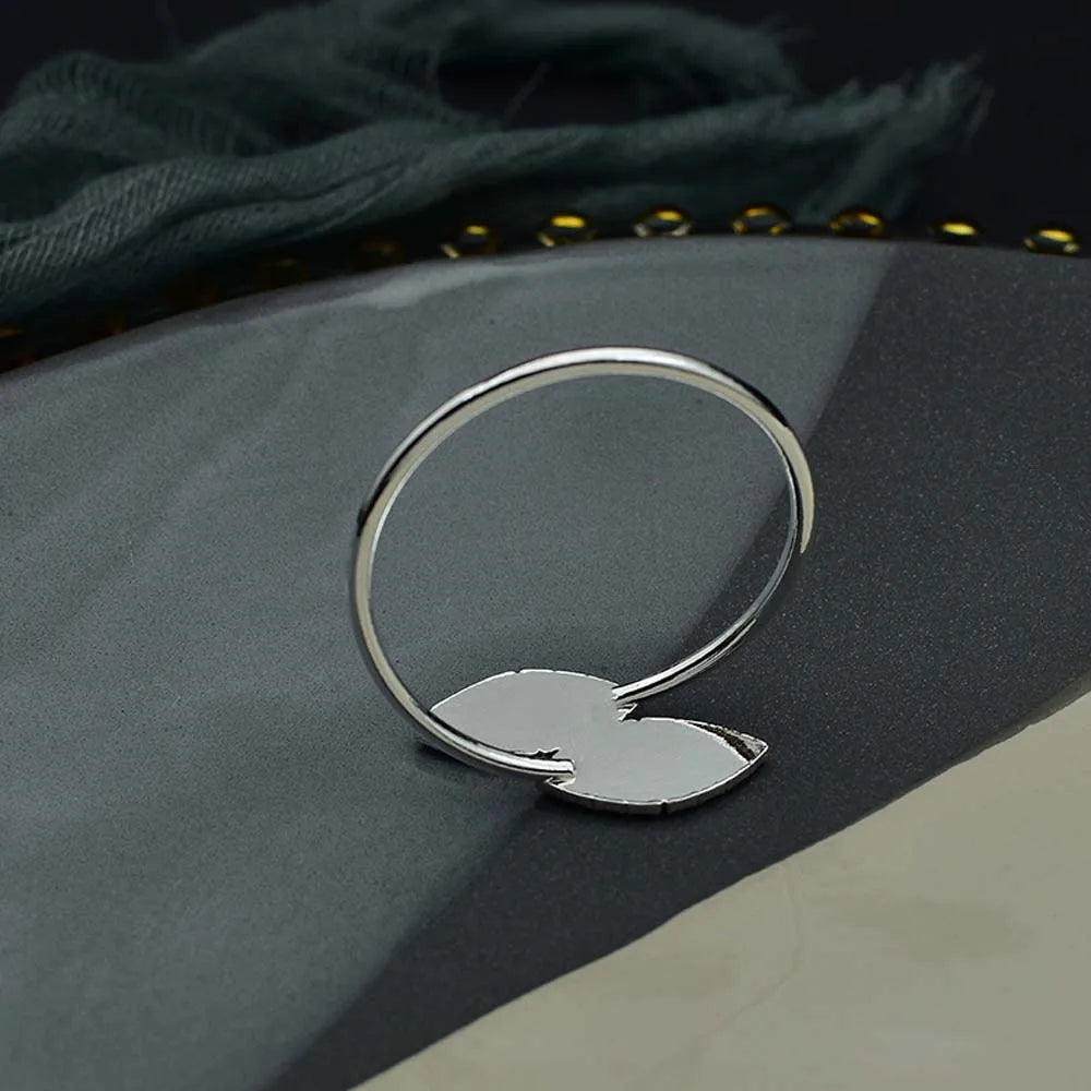 Une bague en métal argent reposant sur un tissu gris foncé avec des détails en relief.