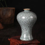 Une délicate vase antique en céramique aux motifs de craquelures subtils, posé sur un support brun foncé, créant une ambiance mystérieuse et élégante.