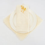 Une assiette et une serviette blanches avec quelques fleurs jaunes posées dessus sur un fond blanc.