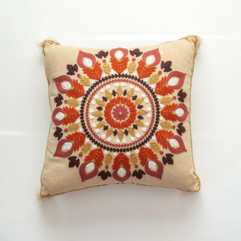 Coussin décoratif beige avec un motif de fleurs et de formes géométriques rouges et jaunes.