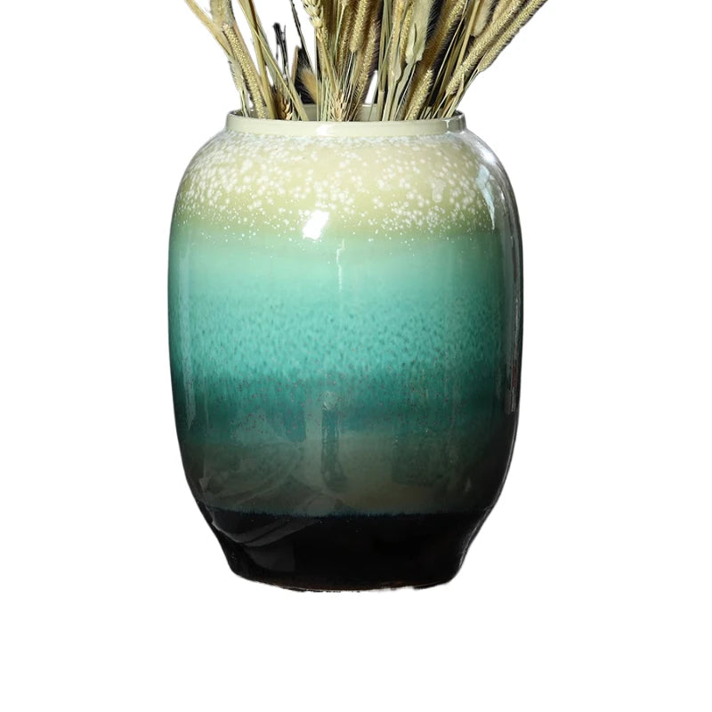 Un vase vintage en verre dégradé de couleurs vertes et dorées, rempli d'épis décoratifs, créant une ambiance naturelle et sereine.