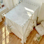 Un lit baldaquin élégant drapé de tissus blancs, placé dans une pièce lumineuse avec un sol en bois.