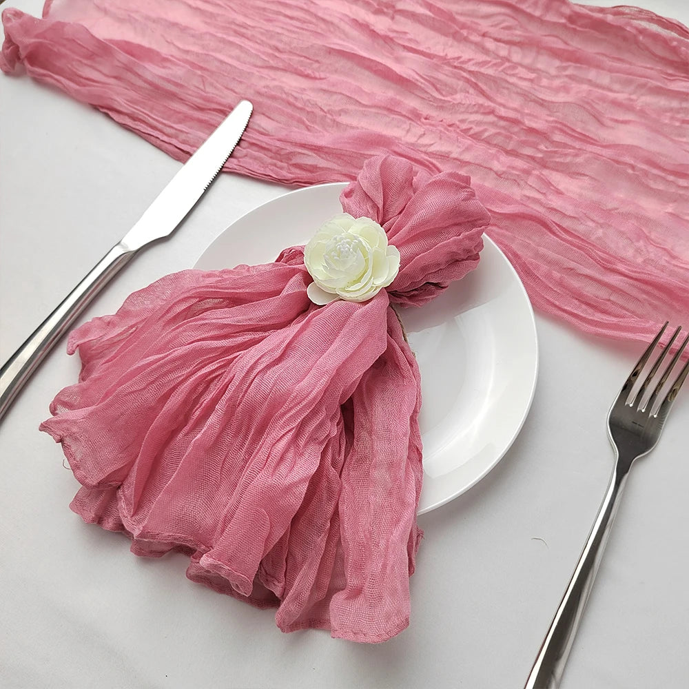 Assiette blanche avec une serviette en tissu froissé de couleur rose clair, décorée d'une rose blanche, accompagnée d'une fourchette et d'un couteau.
