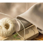 Bobine de fil beige posée sur un morceau de bois avec un tissu beige délicatement drapé, capturant l'élégance et la simplicité naturelle. Idéal pour des projets créatifs et des compositions artisanales raffinées.