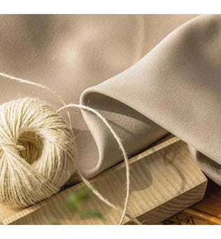 Bobine de fil beige posée sur un morceau de bois avec un tissu beige délicatement drapé, capturant l'élégance et la simplicité naturelle. Idéal pour des projets créatifs et des compositions artisanales raffinées.