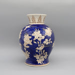 Vase en céramique bleu avec motifs floraux blancs et dorés, créant un contraste élégant et décoratif.