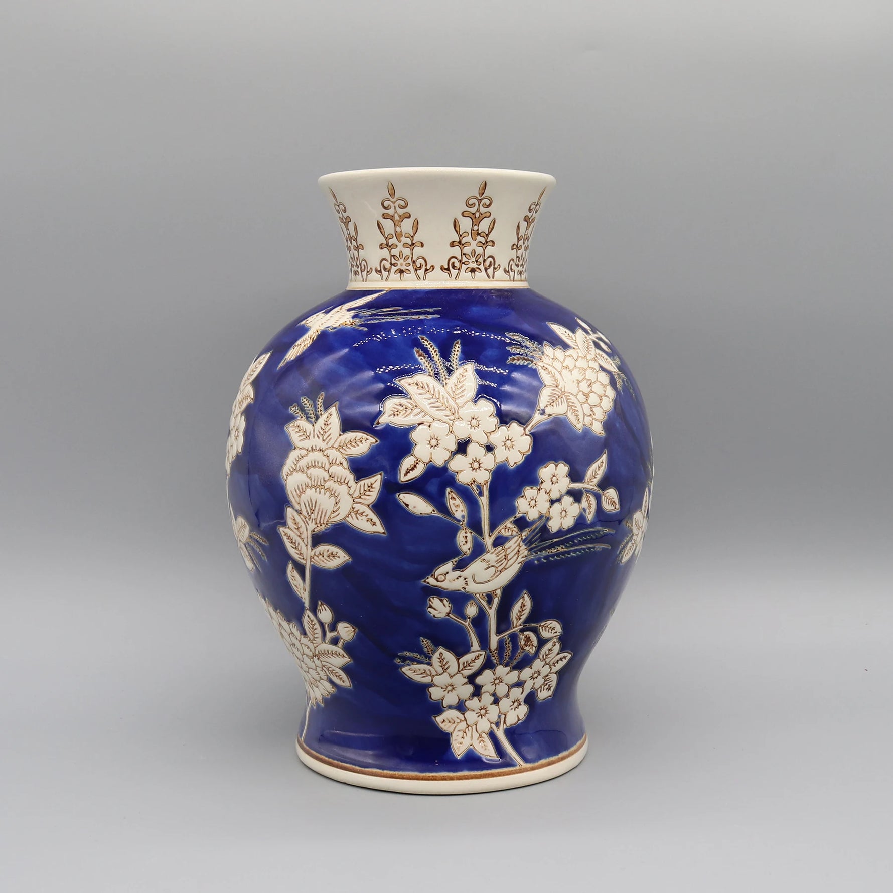 Vase en céramique bleu avec motifs floraux blancs et dorés, créant un contraste élégant et décoratif.