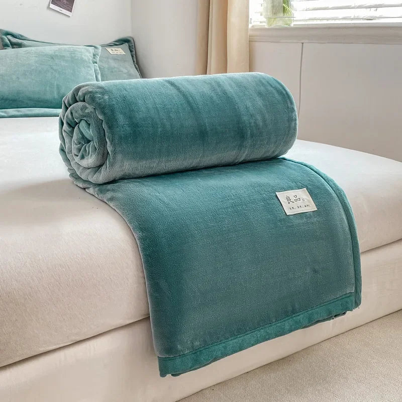 Couverture douce et moelleuse de couleur vert d'eau posée sur un canapé, avec une étiquette visible indiquant la marque.