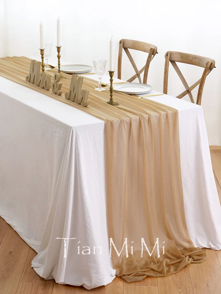 Magnifique table dressée avec nappe blanche, chemin de table doré, chandeliers et chaises en bois, créant une ambiance chaleureuse et élégante.