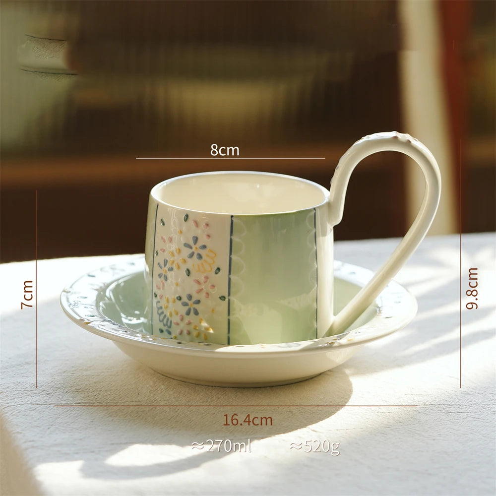 Une tasse de café en céramique blanche et verte avec un motif de fleurs colorées, reposant sur une soucoupe assortie.