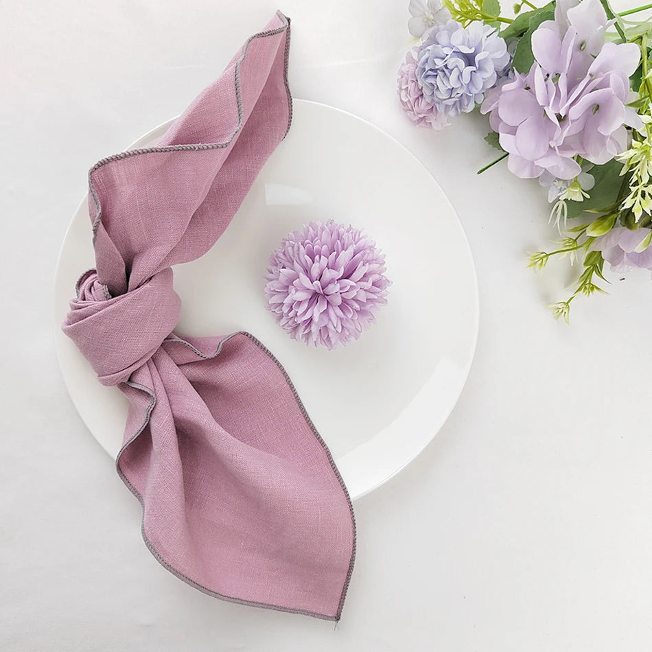 Sur une assiette blanche repose une belle serviette de table rose nouée en nœud, accompagnée de fleurs violettes fraîches.