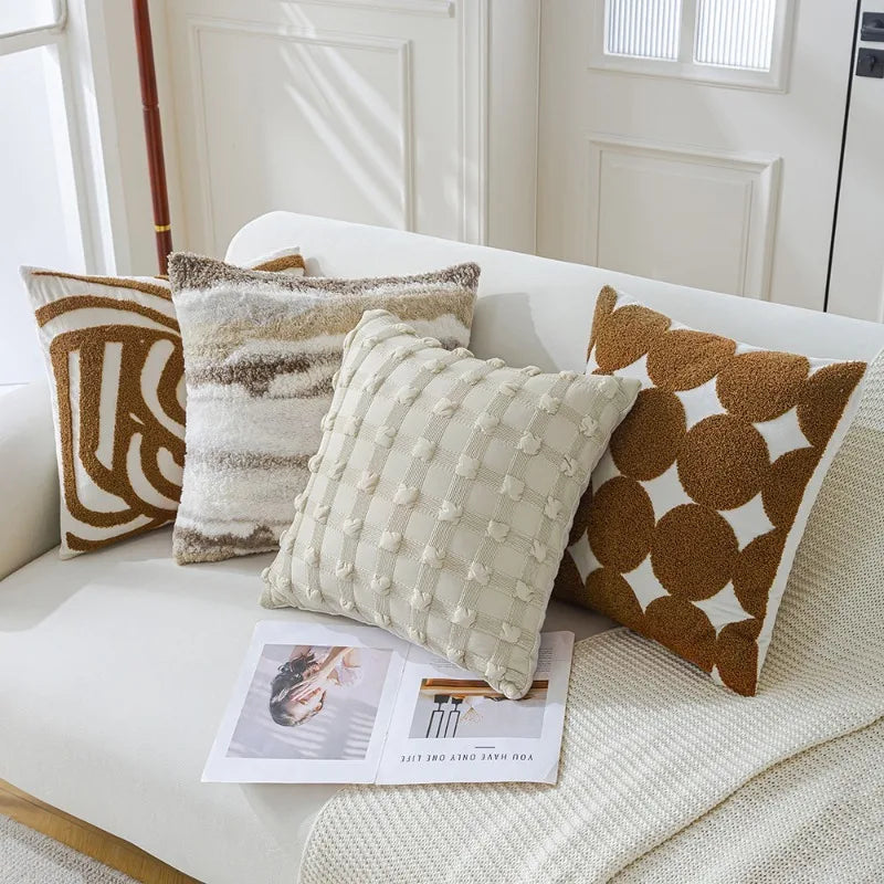 Une collection de coussins décoratifs aux motifs géométriques et textures douces, disposés sur un canapé blanc, évoquant un intérieur confortable et chaleureux.