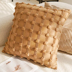 Coussin décoratif en lin beige avec motif à carreaux et pompons, posé sur un canapé dans un intérieur cosy.