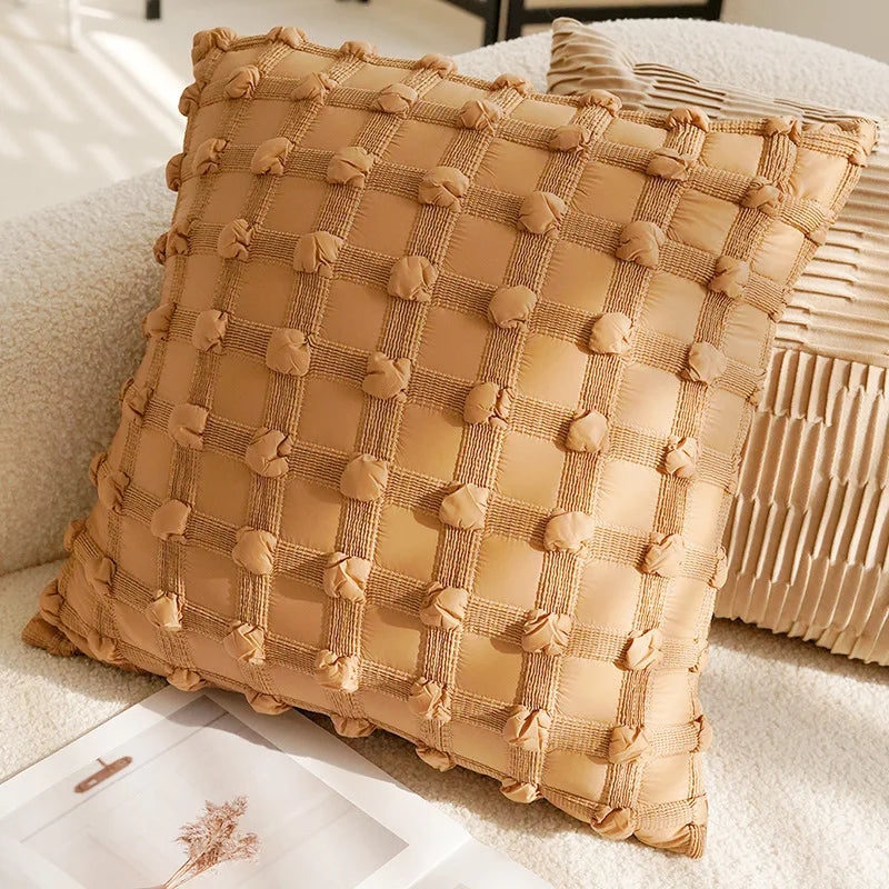 Coussin décoratif en lin beige avec motif à carreaux et pompons, posé sur un canapé dans un intérieur cosy.