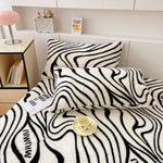 Une chambre moderne avec une couverture à motif zébré noir et blanc posée sur un lit, une lampe rose sur une table de chevet, et des décorations sur une étagère.