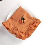Serviette de table en coton orange avec bordure à volants et décoration de petites pommes rouges sur la tête de la table blanche.