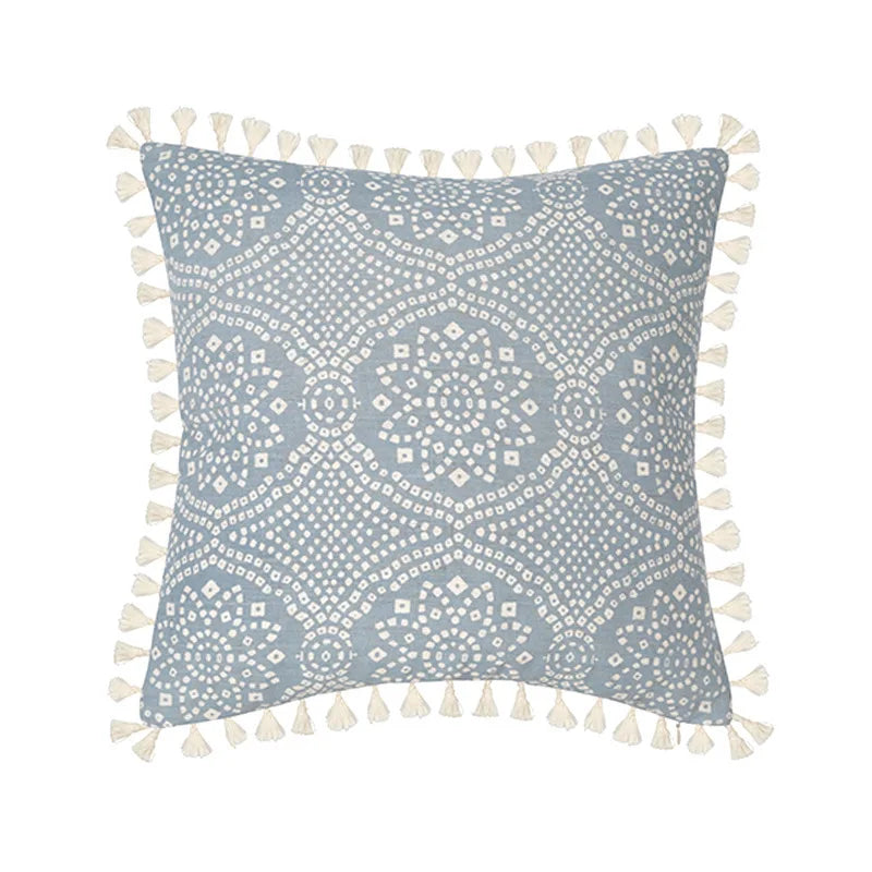 Coussin décoratif gris et blanc avec motifs floraux et pompons.