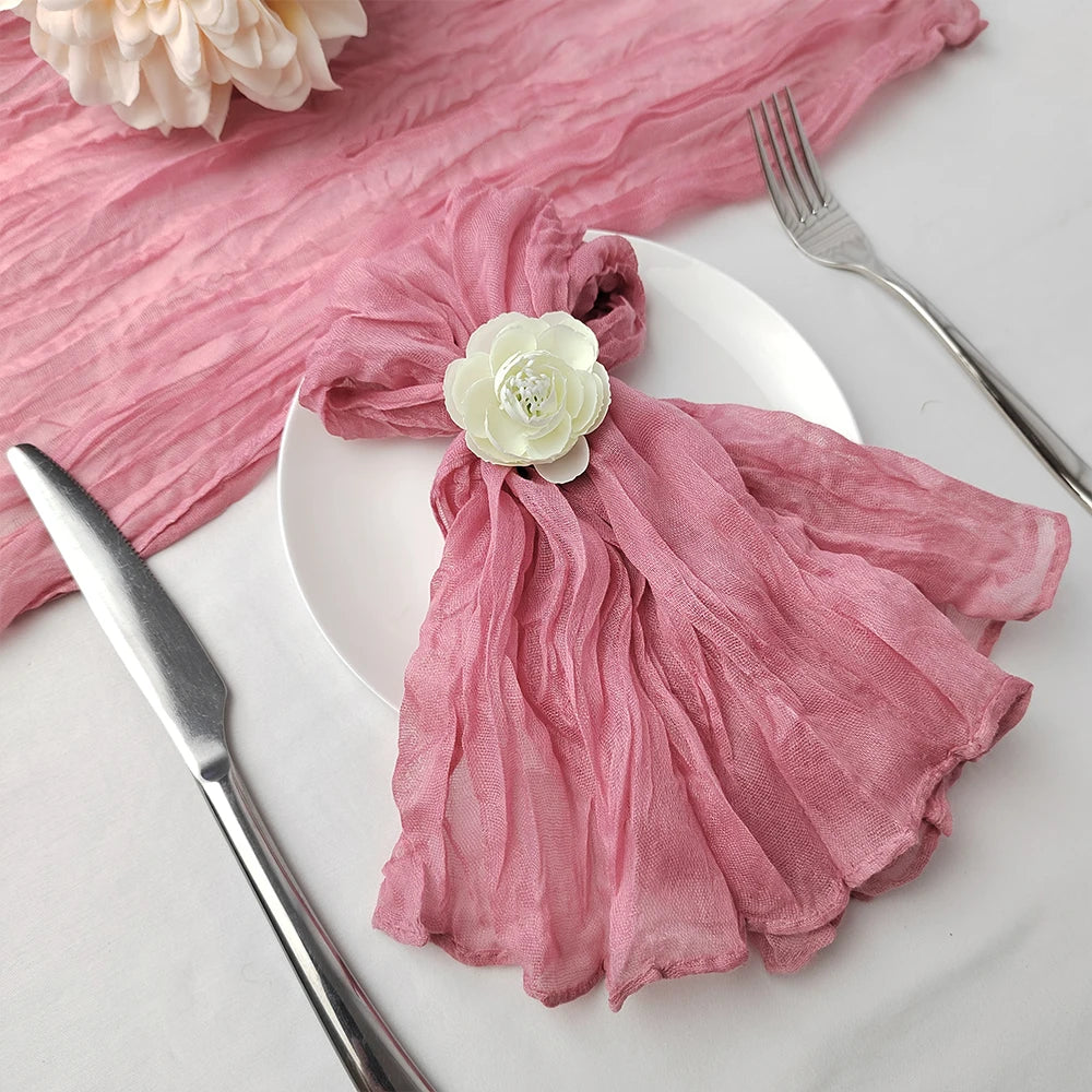 Délicate serviette rose drapée avec un petit bouton de rose blanche, accompagnée d'une fourchette en acier sur une assiette blanche.