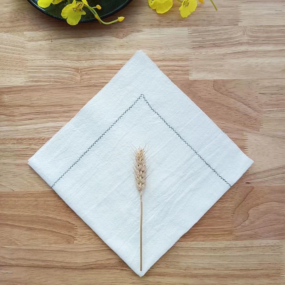Un épi de blé posé délicatement sur un linge blanc, entouré de fleurs jaunes sur un fond en bois, créant une composition minimaliste et apaisante.