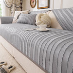 Cette image montre un canapé confortable avec des rayures gris et beige. Il y a un coussin en forme de nœud ainsi qu'une tasse posés sur le canapé, suggérant un lieu cosy et accueillant.