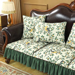 Un canapé en cuir marron avec des oreillers décoratifs à motifs floraux et des oiseaux sur fond beige, ainsi qu'un joli tapis de sol et une lampe de table vintage complètent cette scène chaleureuse et élégante.