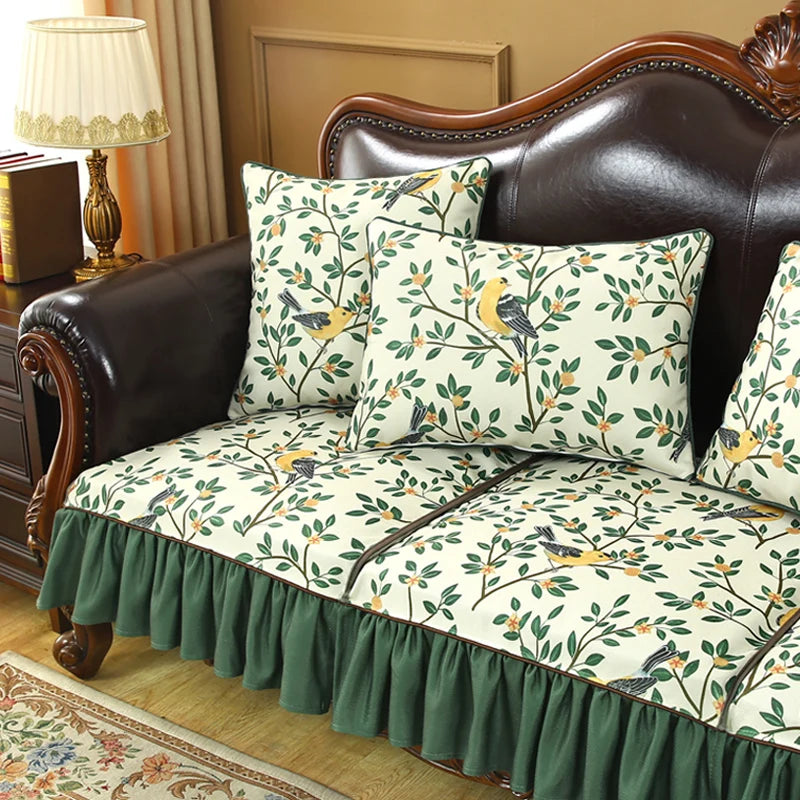 Un canapé en cuir marron avec des oreillers décoratifs à motifs floraux et des oiseaux sur fond beige, ainsi qu'un joli tapis de sol et une lampe de table vintage complètent cette scène chaleureuse et élégante.