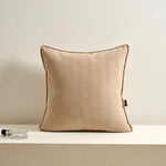 Coussin décoratif beige en tissu texturé, posé sur une surface blanche.