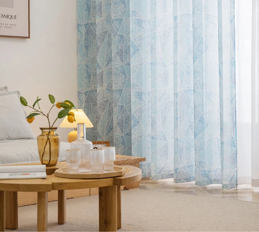 Voilage bleu géométrique installé sur une grande baie vitrée dans un intérieur épuré.