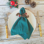 Une nappe de Noël avec une serviette enroulée et décorée de cônes de pin et de baies rouges sur une table en bois.