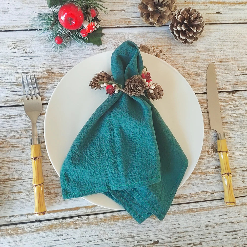 Une nappe de Noël avec une serviette enroulée et décorée de cônes de pin et de baies rouges sur une table en bois.