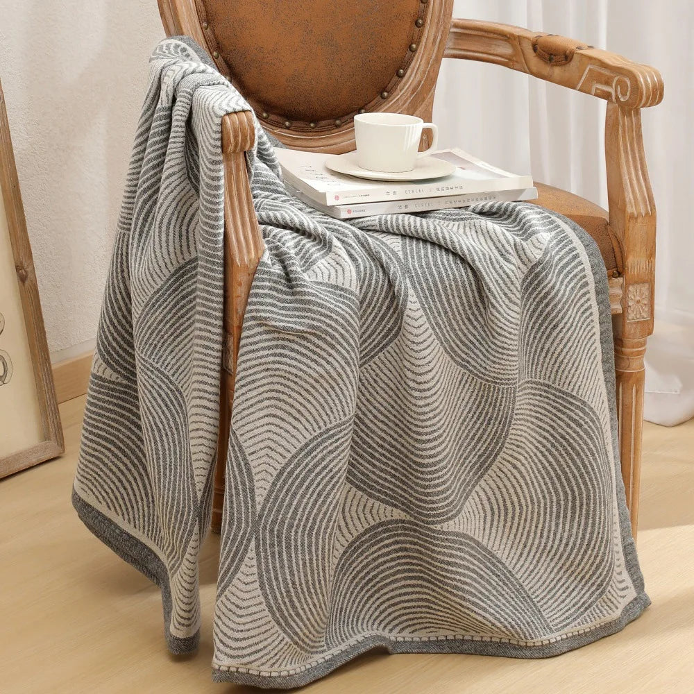 Couverture grise et blanche à motif de rayures déposée sur un fauteuil en bois.