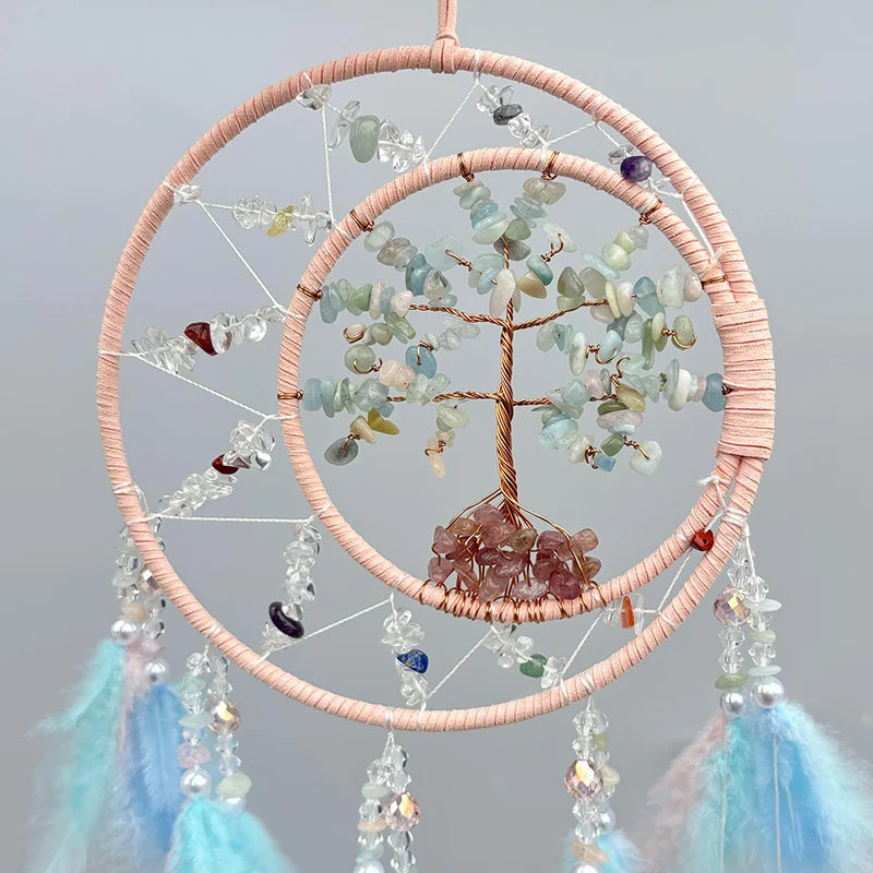 Un magnifique attrape-rêves aux pierres semi-précieuses multicolores, entouré de fines cordes rose pâle et orné d'un arbre de vie en métal doré.