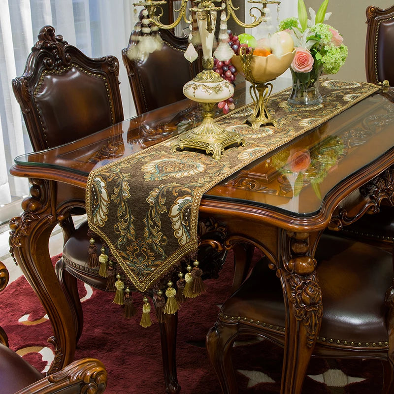 Une salle à manger élégante meublée de chaises sculptées, d'un table en bois massif ornée d'un chemin de table brodé de motifs dorés, et complétée de décorations florales et de chandeliers en laiton.